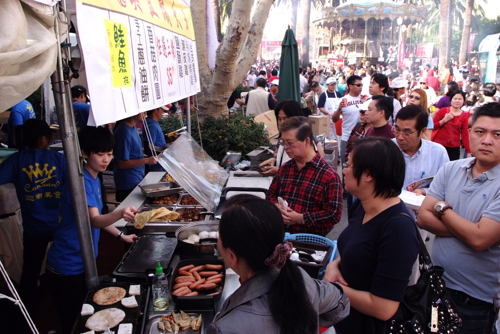 Outdoor food vendor stall with a long menu banner and a crowd of visitors