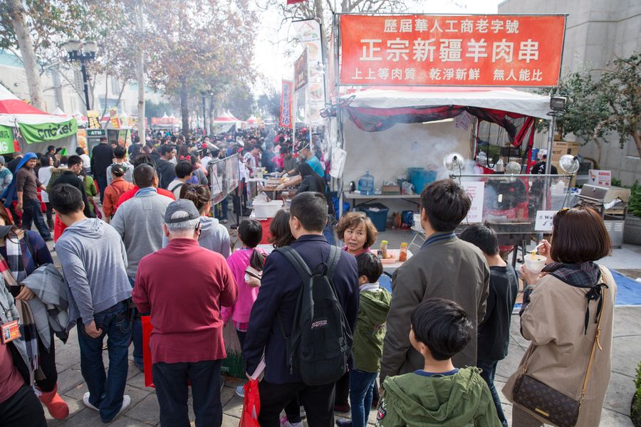 Food vendor tent along a palm-lined outdoor street packed with visitors